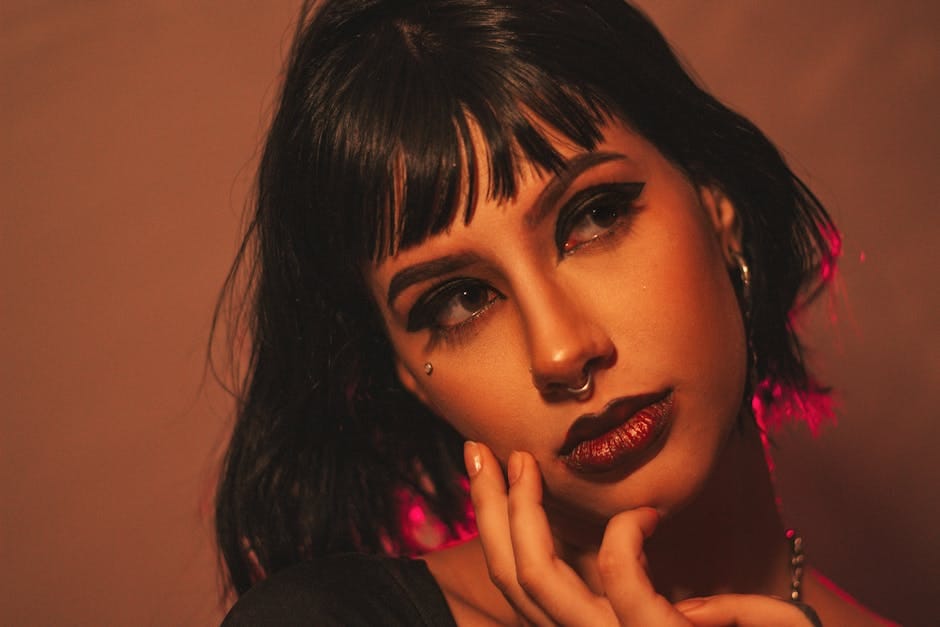 Portrait of a woman with piercing, dark makeup, and black hair in a studio setting.